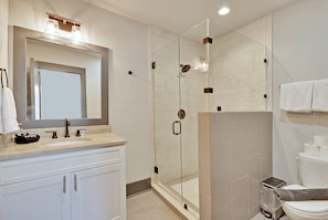 A modern bathroom with a glass-enclosed shower, a large mirror, and a toilet with a towel rack. - The Cooper Suite (Charleston)