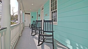Une véranda avec des fauteuils à bascule et une balustrade blanche.