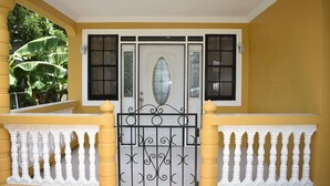 Ein gelbes Haus mit einer weißen Tür, einem schwarzen Tor und einem weißen Balkon.