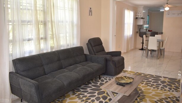 Ein Wohnzimmer mit grauem Sofa, einem passenden Sessel, einem Couchtisch mit Dekoration und einem gemusterten Teppich.