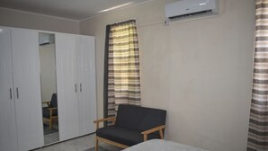 Ein Schlafzimmer mit Bett, Kleiderschrank, Sessel und einem Fenster mit Vorhängen.