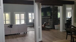 A spacious living room with a white sofa, a stone fireplace, and a dining area with a table and chairs. - Secluded Cove and Dock at Tim's Ford (Winchester)