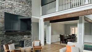 A spacious living area with a stone fireplace, a flat-screen TV, and a dining area with a high ceiling and exposed wooden beams. - Secluded Cove and Dock at Tim's Ford (Winchester)