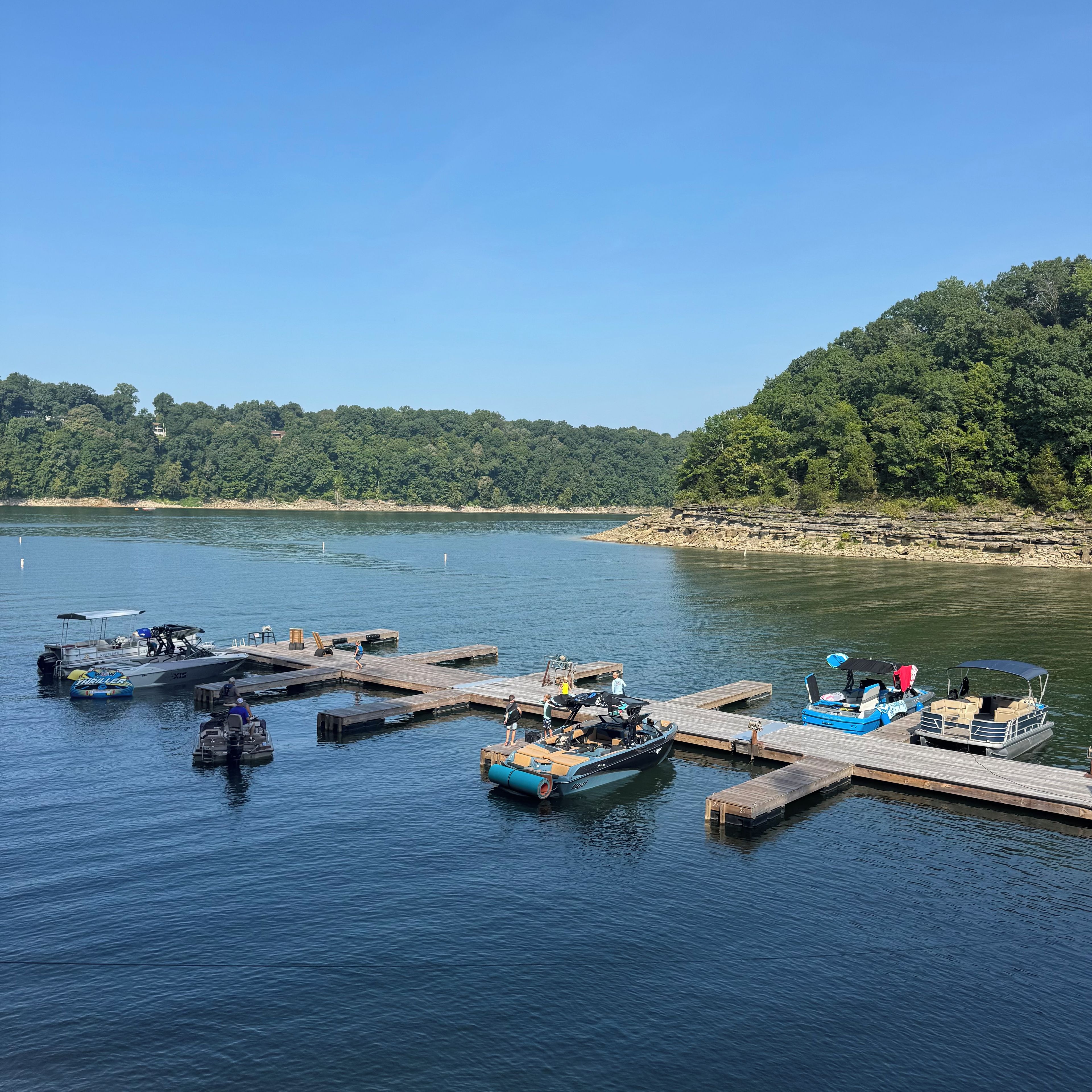 Un port de plaisance où des bateaux sont amarrés à des quais en bois, le tout étant bordé d’une rive boisée.