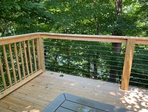 Una terraza de madera con barandilla metálica, rodeada de árboles.