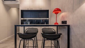 Une cuisine moderne dotée d’un îlot central, de deux tabourets de bar noirs et d’une suspension rouge.