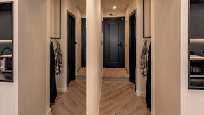 Un couloir doté d’un plancher en bois, de portes noires et d’un porte-manteau sur lequel sont suspendus des vêtements.