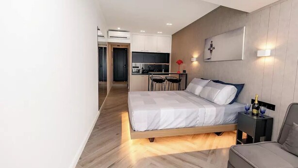 Une chambre à coucher moderne avec un lit en bois, une petite table de chevet sur laquelle se trouvent une bouteille et des verres, et une chaise.