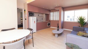 Un salon moderne comprenant une table à manger et des chaises, un canapé gris, une petite table basse et un coin cuisine avec un four à micro-ondes et un réfrigérateur.