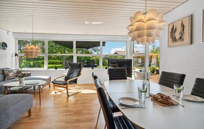 Uma área de jantar moderna com uma mesa grande, cadeiras de couro preto e vista do jardim através de grandes janelas.