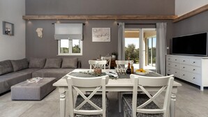 Een moderne woonkamer met een grijze bank, een witte eettafel met stoelen, een televisie en een balkon met uitzicht.