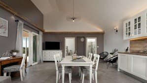 Een moderne keuken met witte kasten, een eettafel met stoelen, een televisie en een plafondlamp.