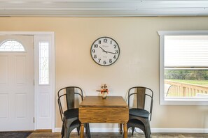 Un comedor con mesa de madera, dos sillas, un reloj de pared y una ventana con persianas.