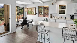 A modern kitchen with white cabinets, a central island, and a dining area with black chairs.