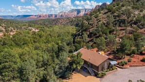 A house with a garage, surrounded by dense green trees and a red rock mountain in the background.
