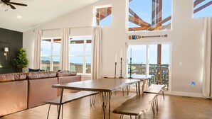 A spacious living area with a long dining table, a comfortable seating arrangement, and large windows offering views of the cityscape. - Timeless Lake Views, Indoor Pool, Game Room, Hot tub, Firepit, Minutes from SDC (Branson)