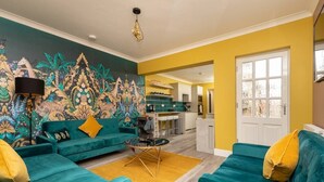 A living room with teal sofas, a yellow rug, and a vibrant mural on the wall.