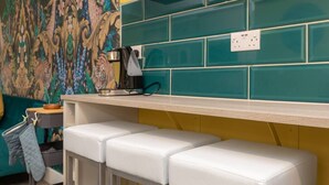 A kitchen with teal tiles, a coffee maker on the counter, and white bar stools.