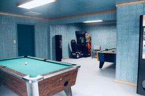 A pool table with a green felt surface, a pool cue, and a white cue ball. There is a door on the left and a wall with a textured pattern.