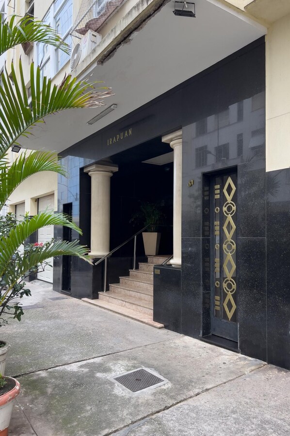 Fachada de un edificio con un letrero que dice "IRAPUAN", una escalera que conduce a la entrada y una puerta decorativa con diseños geométricos.
