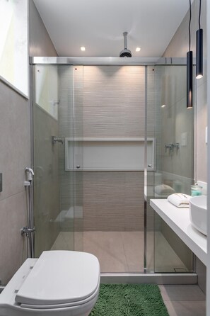 Un baño moderno con ducha de mampara de vidrio, inodoro blanco y alfombra verde.