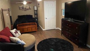 Une chambre à coucher comprenant un lit, une commode, un téléviseur, un ventilateur de plafond et une porte.