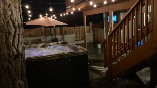 Un bain à remous avec une terrasse en bois et des guirlandes lumineuses, un escalier en bois et un espace salon abrité.