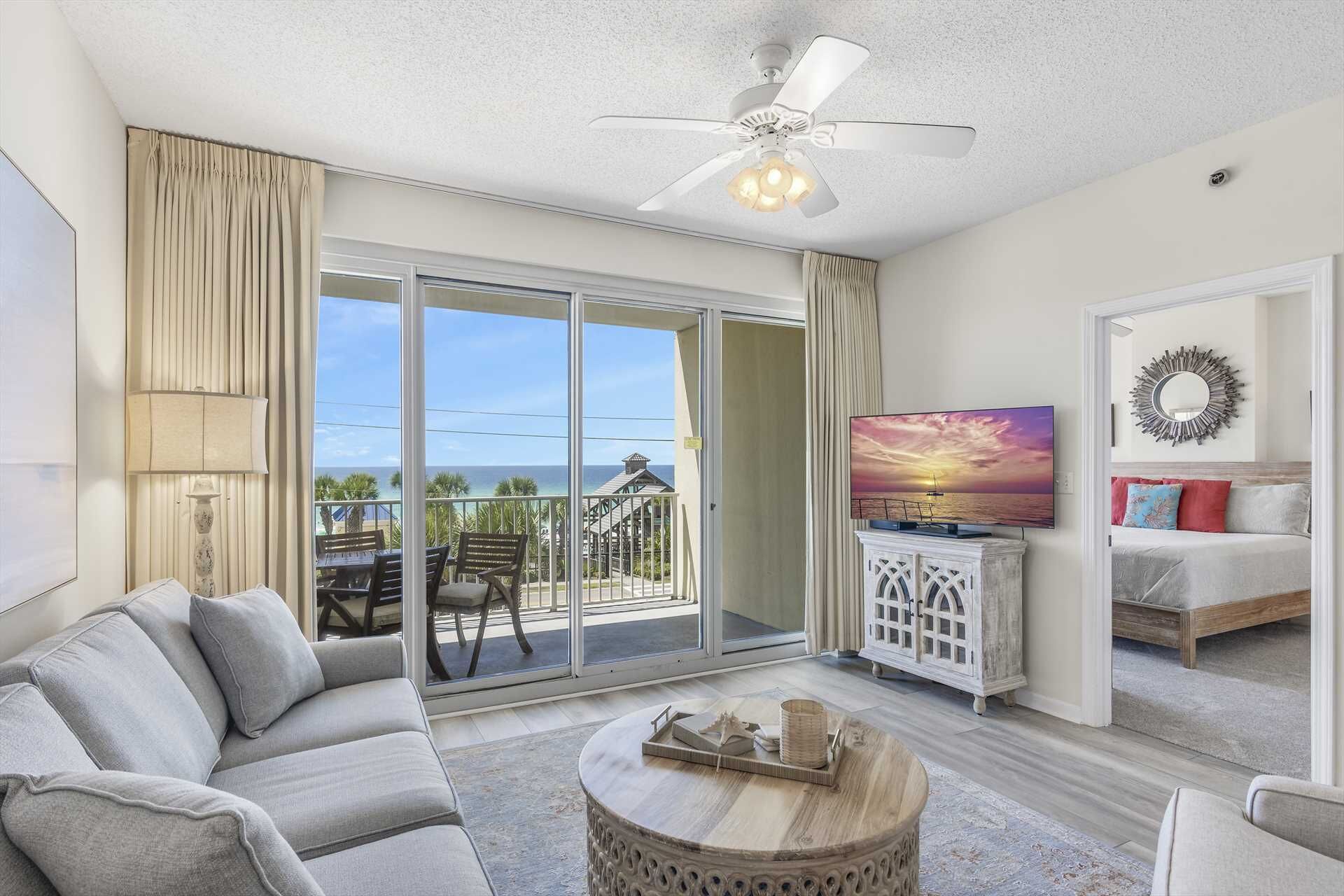 A living room with a sofa, a coffee table, a TV, and a balcony with a view of the ocean.