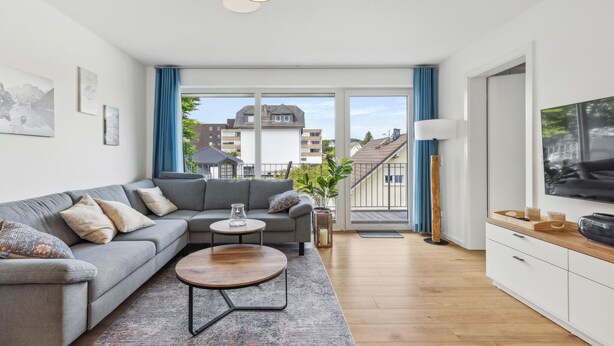 A modern living room with a grey sofa, a round coffee table, and a TV on the right. - GebirgsResort Winterberg (Winterberg)