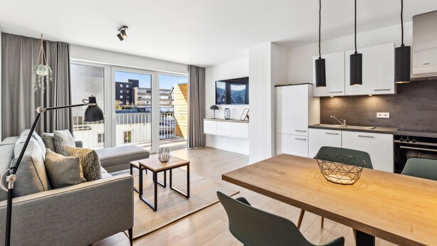 Un appartement moderne comprenant un coin repas, une cuisine et un balcon avec vue sur les immeubles.