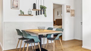 Un espace repas moderne avec une table en bois et des chaises de couleur turquoise, un luminaire suspendu et une plante posée sur une étagère.