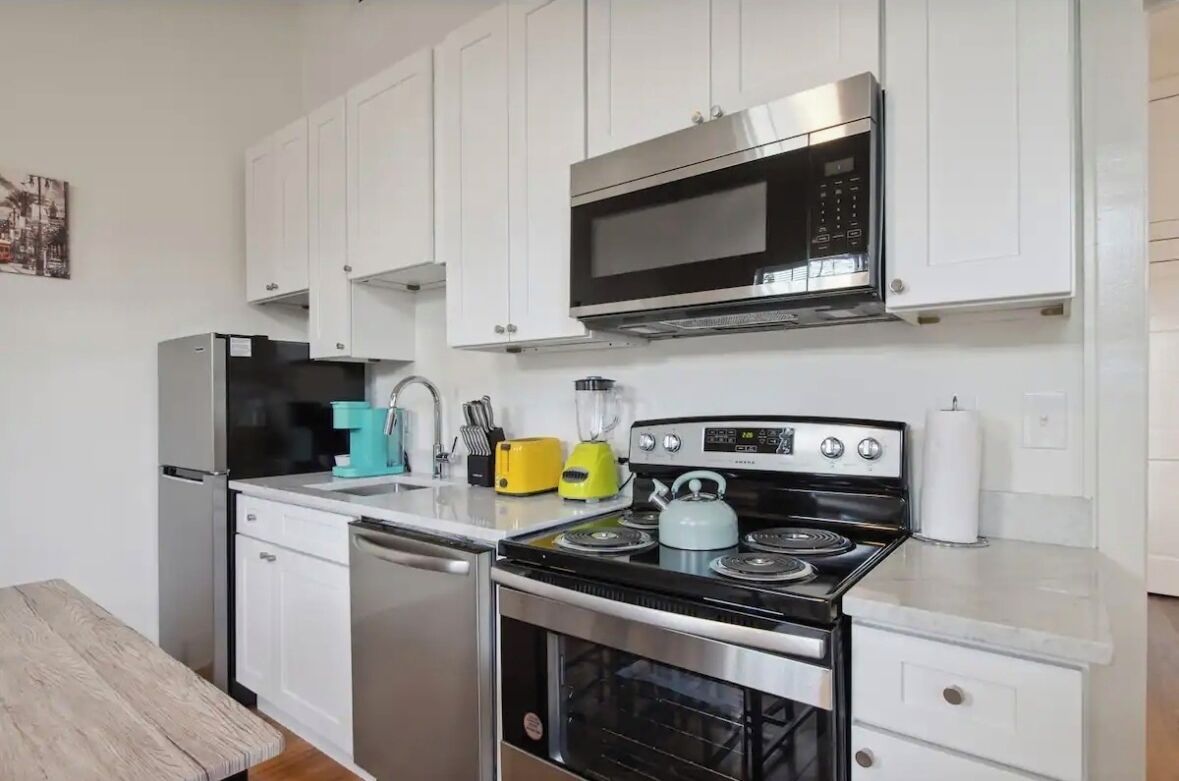 Una cocina moderna con armarios blancos, electrodomésticos de acero inoxidable, microondas, estufa y lavavajillas.