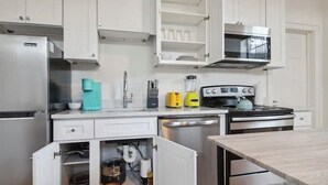 Uma cozinha moderna com armários brancos, uma geladeira de aço inoxidável, micro-ondas, fogão e lava-louças.