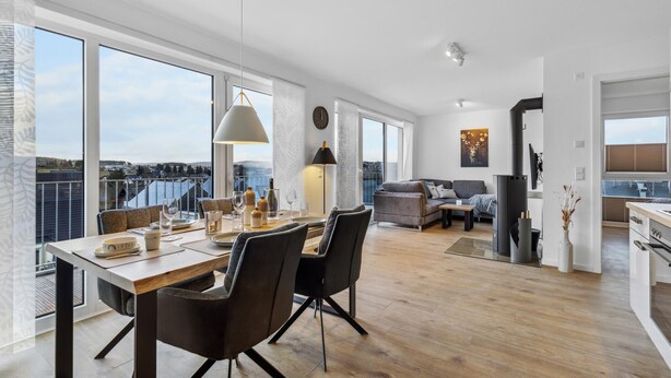 Un vaste espace de vie comprenant une table à manger, des chaises et un canapé. Une grande fenêtre offre une vue sur le paysage urbain.