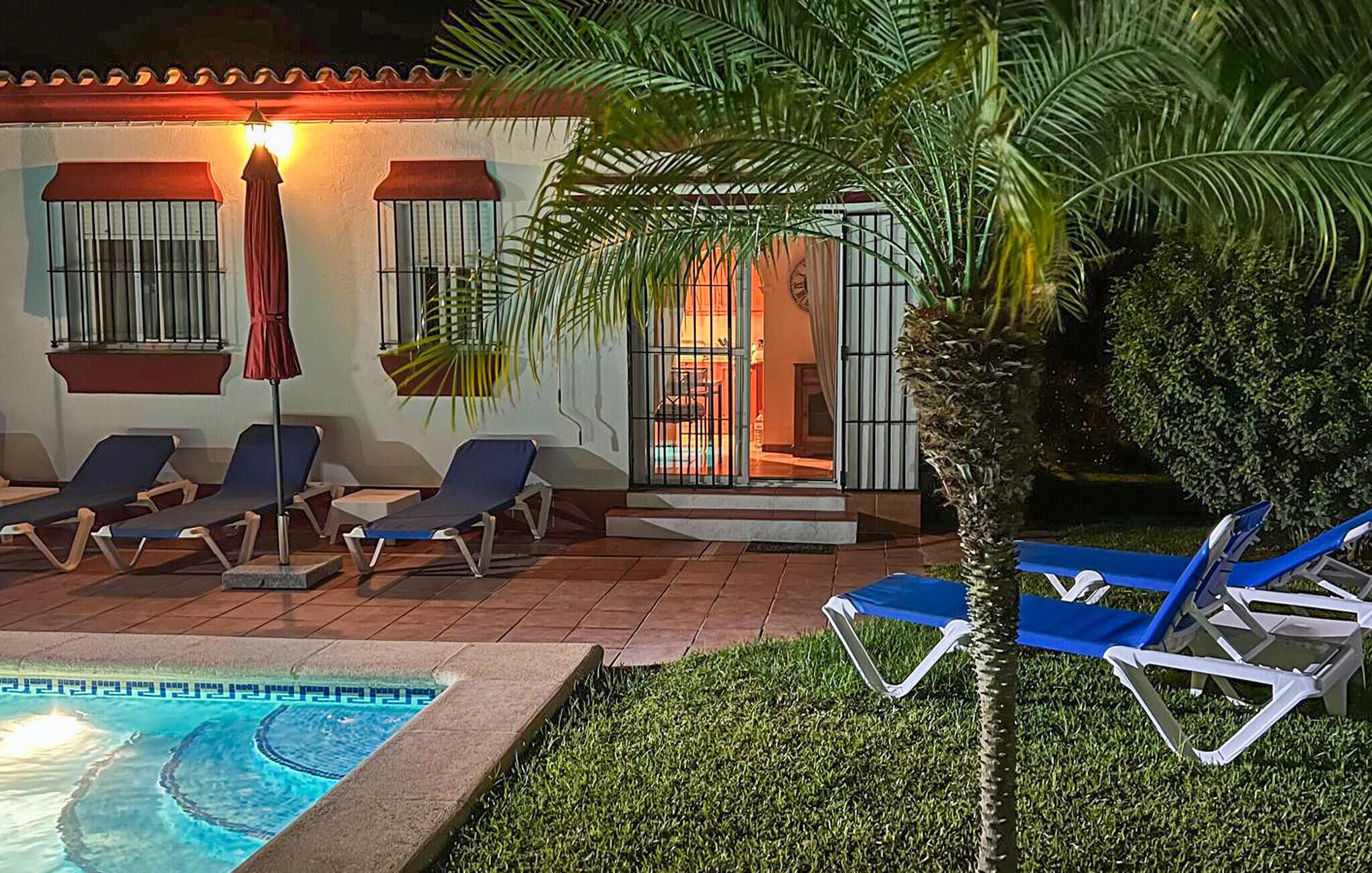 Un espace aménagé au bord de la piscine, avec des chaises longues, une petite piscine et un bâtiment dont les fenêtres sont protégées par des barreaux et qui est surmonté d’un auvent rouge.