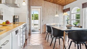 Cuina moderna amb armaris blancs, taulell de fusta i zona de dinar amb cadires negres i un gran taula.