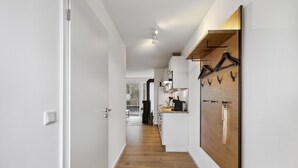 A hallway with a wooden floor leading to a kitchen area with a wooden wall-mounted coat rack. - GebirgsResort Winterberg (Winterberg)