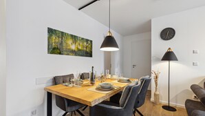 A modern dining area with a wooden table, dark upholstered chairs, and pendant lighting. - GebirgsResort Winterberg (Winterberg)