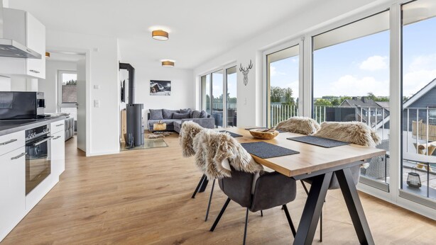 Eine moderne Küche mit Herd, Backofen und Kaffeemaschine. Ein Essbereich mit Tisch, Stühlen und Blick ins Freie.