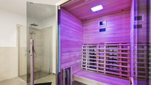 Ein Saunaraum mit Holzwänden, einer Sitzbank, einer Glasdusche und einem Bedienfeld an der Wand.