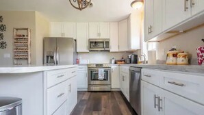 Una cocina con armarios blancos, electrodomésticos de acero inoxidable y piso de madera.