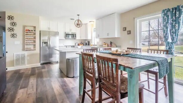 Una cocina moderna con armarios blancos, electrodomésticos de acero inoxidable y una zona de comedor con sillas y mesa de madera.