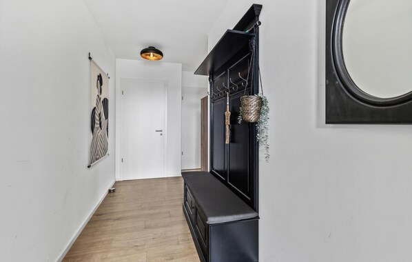Ein Flur mit Holzboden, einer Bank, einem schwarzen Schrank mit Haken, einem hängenden Korb und einem gerahmten Bild an der Wand.
