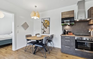 Una cocina moderna con horno Siemens, un comedor con mesa de madera y sillas grises, y una cama en la habitación contigua.