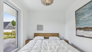 Un dormitorio con una cama grande, cabecera de madera, un cuadro en la pared y vista a una casa por la ventana.