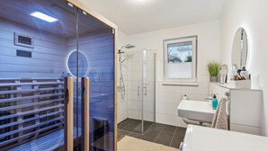 Un baño moderno con sauna de vidrio, zona de ducha, lavamanos y espejo.