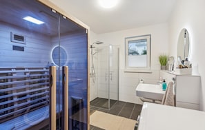 A modern bathroom with a glass-enclosed sauna, a shower area, a sink, and a mirror.