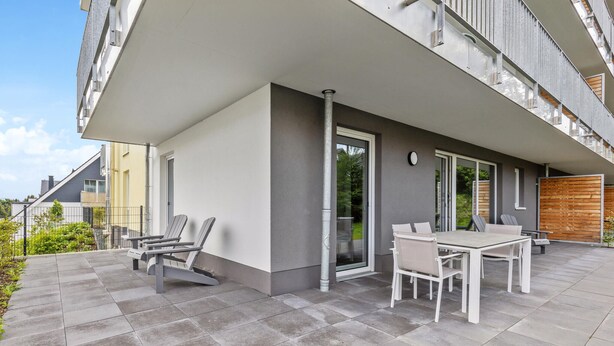Un patio moderno al aire libre con una mesa, sillas, una puerta corredera de vidrio y vistas del vecindario circundante.