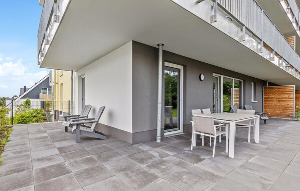 A modern outdoor patio with a table and chairs, a sliding glass door, and a view of the surrounding neighborhood.