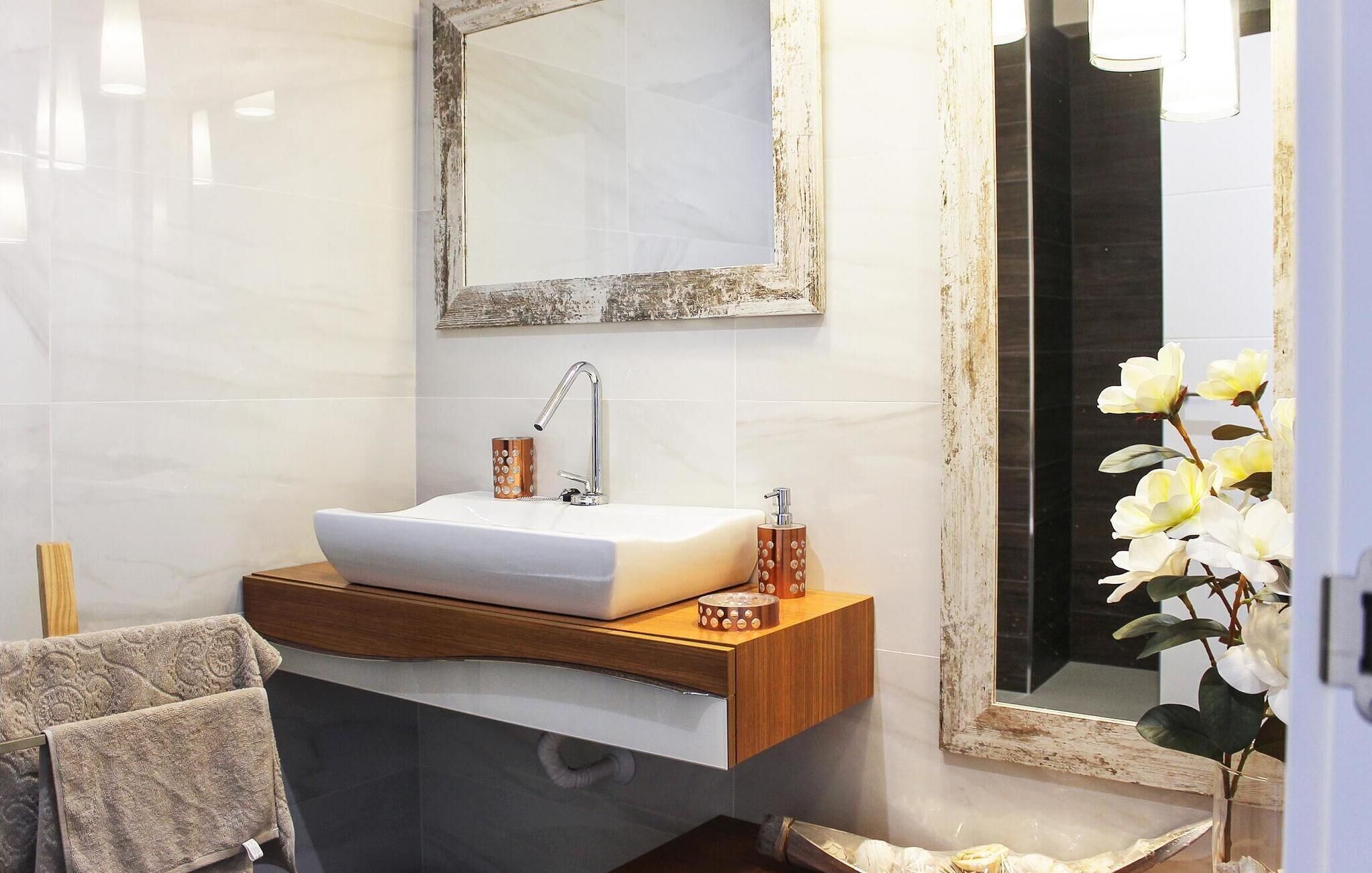 Une salle de bain avec un lavabo blanc, un meuble-lavabo en bois et un miroir dont le cadre est vieilli.